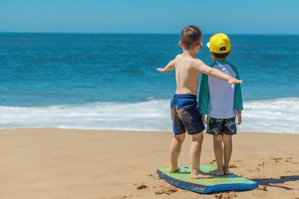 Two children playing on a boogie board at the beach on a sunny day.